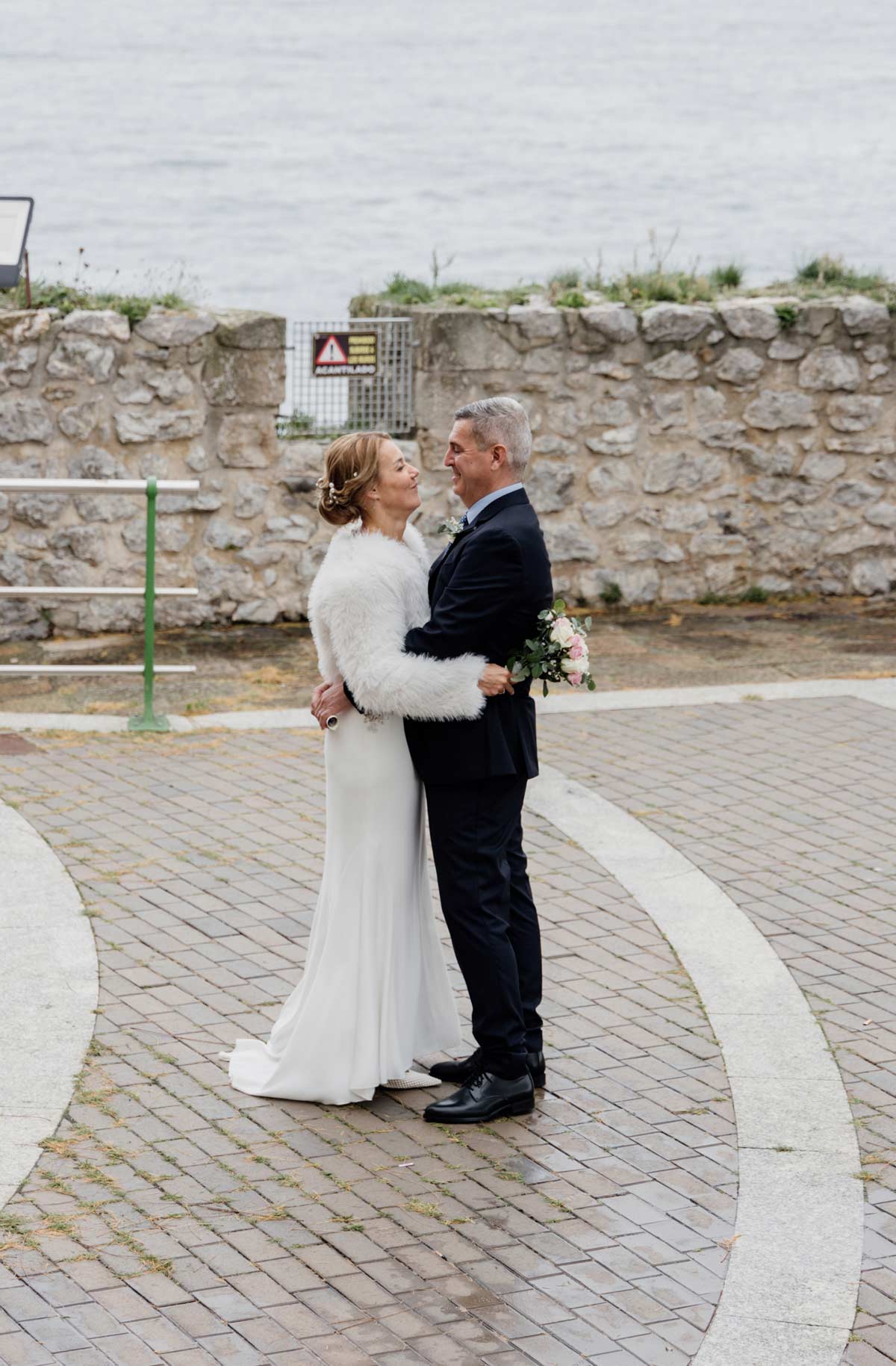 Pareja de recién casados abrazándose у mirándose en un entorno costero con el mar al fondo en Cantabria.
