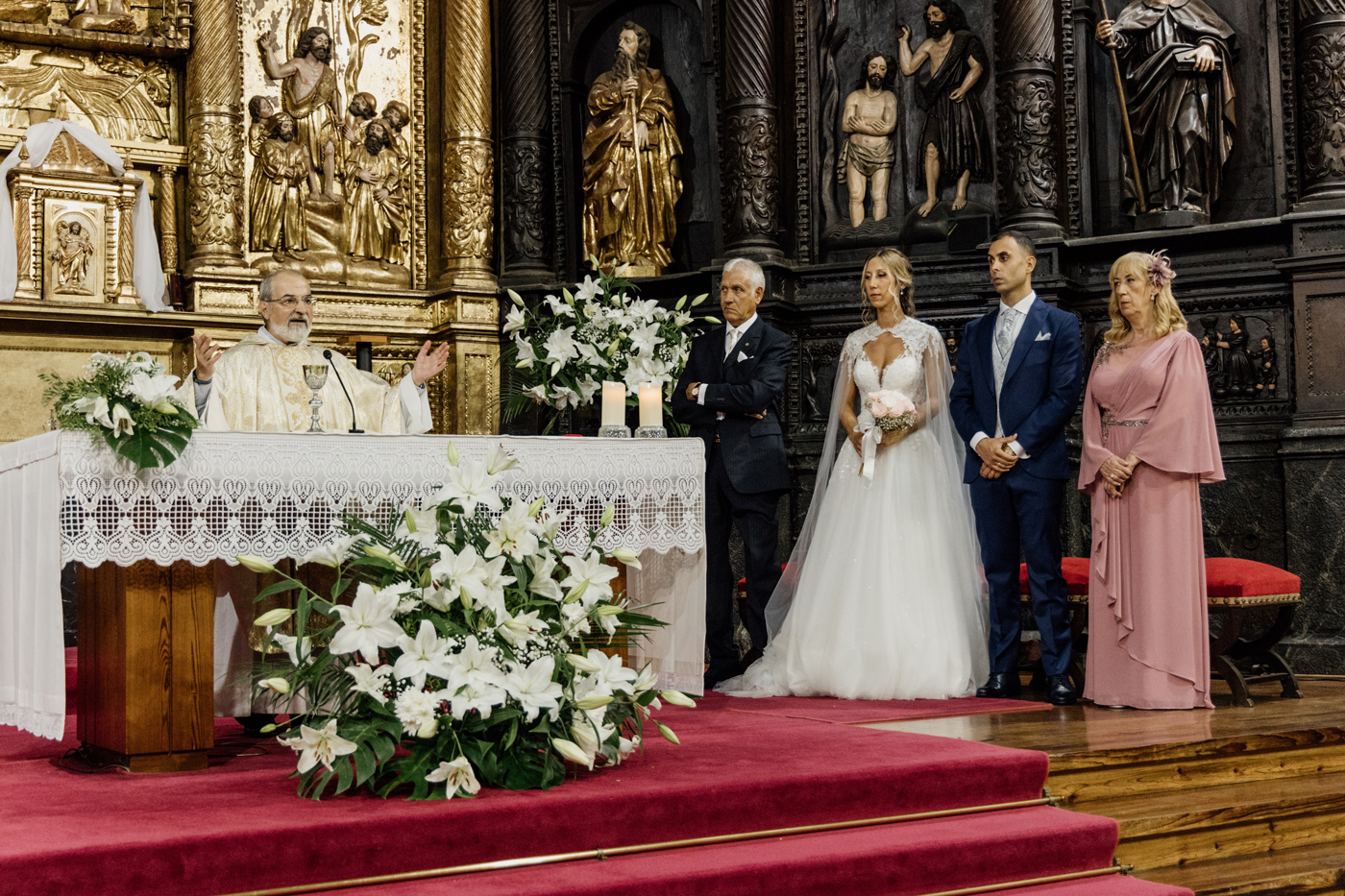Ceremonia de boda en una iglesia con el sacerdote en el altar y los novios acompañados de familiares, fotografiada por un fotógrafo de bodas en Bilbao.