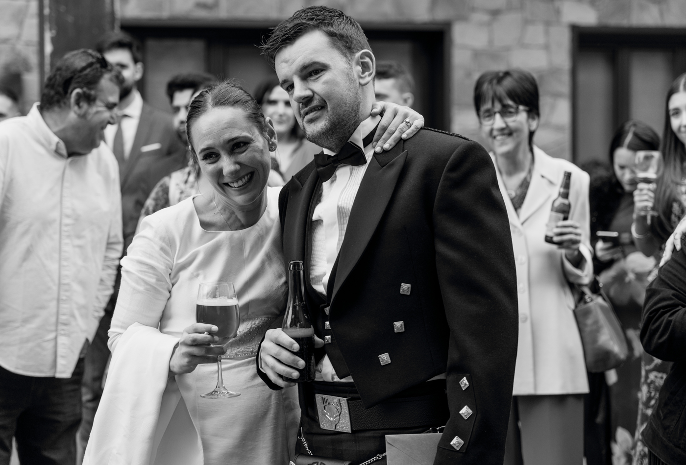 Pareja de recién casados abrazándose y celebrando con los invitados durante el cóctel, fotografía en blanco y negro realizada por un fotógrafo de bodas en Bizkaia.