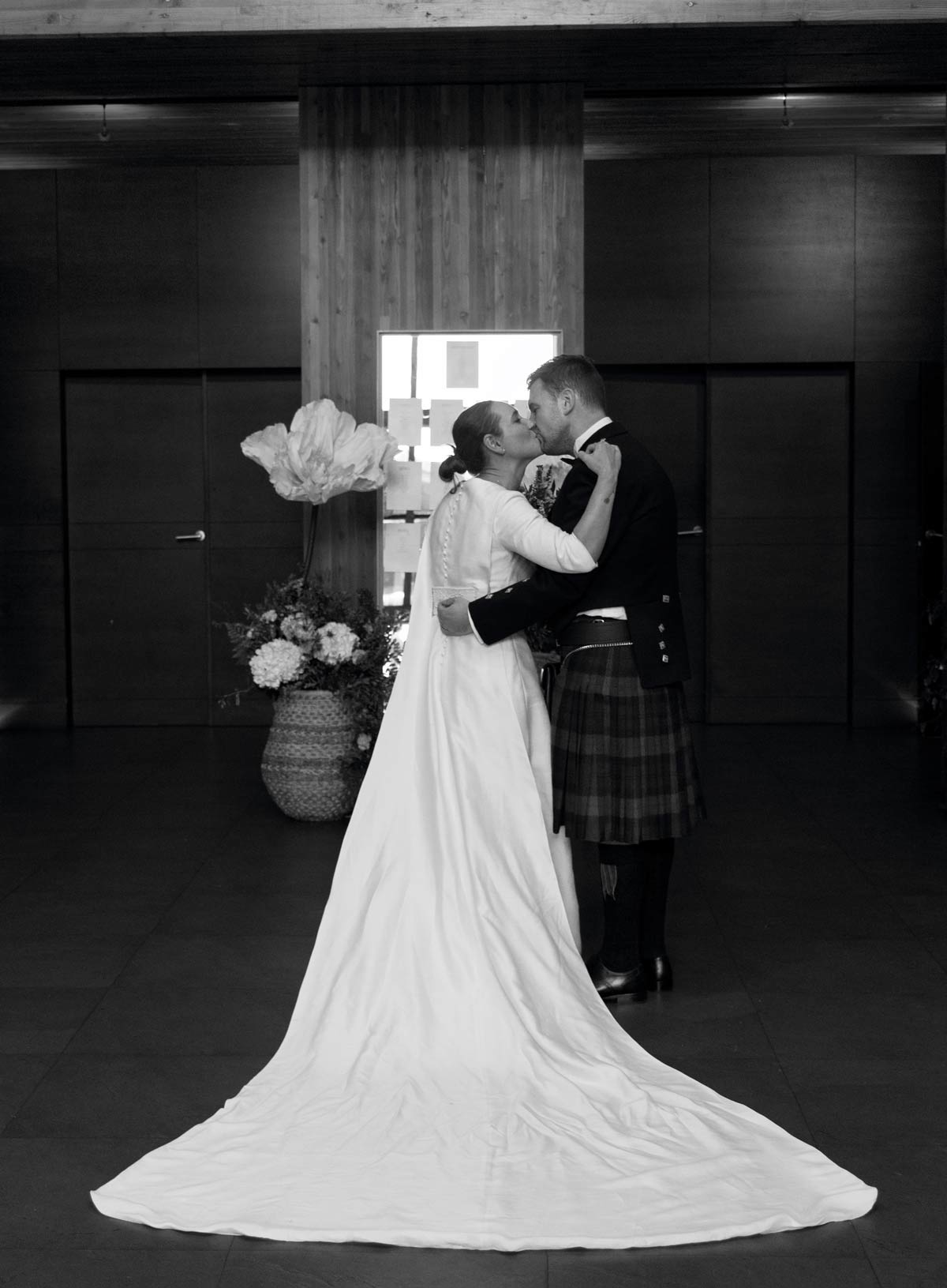 Pareja de recién casados besándose en un interior elegante, fotografía en blanco y negro realizada por un fotógrafo de bodas en Bizkaia.