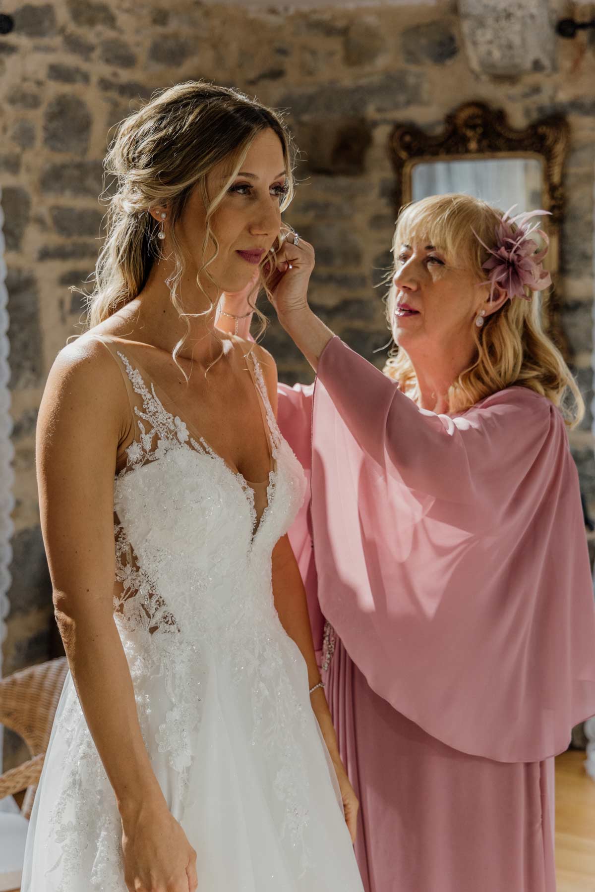 Mujer ayudando a la novia a colocarse los pendientes durante los preparativos de la boda, fotografiado por un fotógrafo de bodas en Bilbao.
