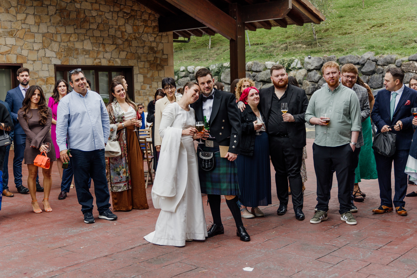 Invitados y pareja de recién casados disfrutando del cóctel al aire libre en un espacio rústico de piedra.