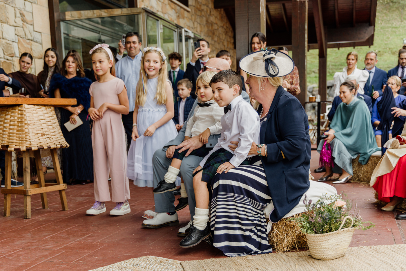 Grupo de invitados y niños esperando durante una boda al aire libre en un espacio rústico con piedra.