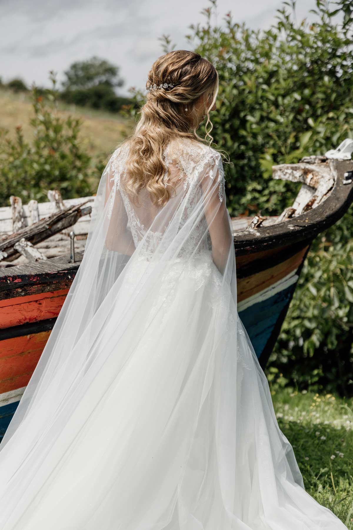 Novia de espaldas con velo largo posando junto a una barca en un entorno natural, fotografiada por un fotógrafo de bodas en Bilbao.